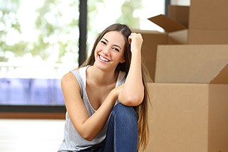 Smiling woman sitting on the floor next to cardboard moving boxes indoors