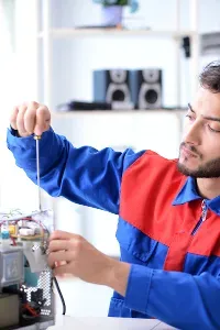Man in blue and red uniform with a screwdriver repairing an appliance.