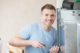 Man repairing air conditioning unit with a screwdriver in a home setting