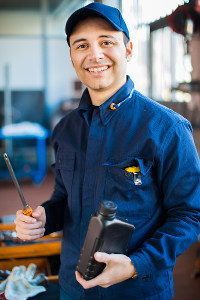 mechanic in a blue uniform and cap holding a screw driver and container of oil