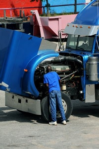 Diesel mechanic performing maintenance on a semi-truck engine with the hood open