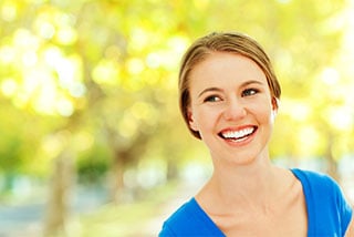 Happy young woman smiling in a park with green trees in the background