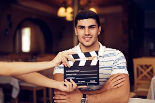 Young male filmmaker holding a clapperboard with a smile in a well-lit indoor setting
