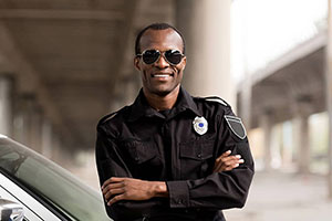 A confident security officer wearing sunglasses and a uniform, standing near a vehicle.