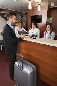 Man checking into hotel at reception desk with three female staff members assisting him.