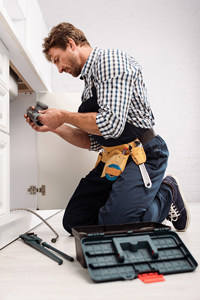 Plumber fixing a kitchen sink pipe with tools nearby