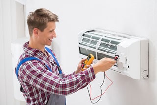 Smiling technician repairing air conditioner with screwdriver.