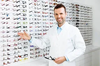 Male optician in white coat presenting a selection of eyeglasses in a store.